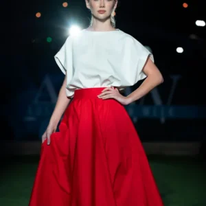 Model in a striking white top and flowing red skirt on runway.