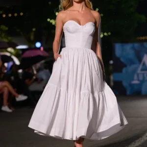 Model walks runway in elegant white strapless dress at fashion show.