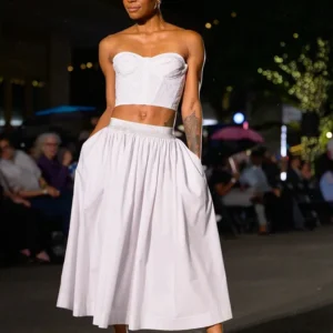 Model wearing a white bandeau top and flowing white skirt on runway.