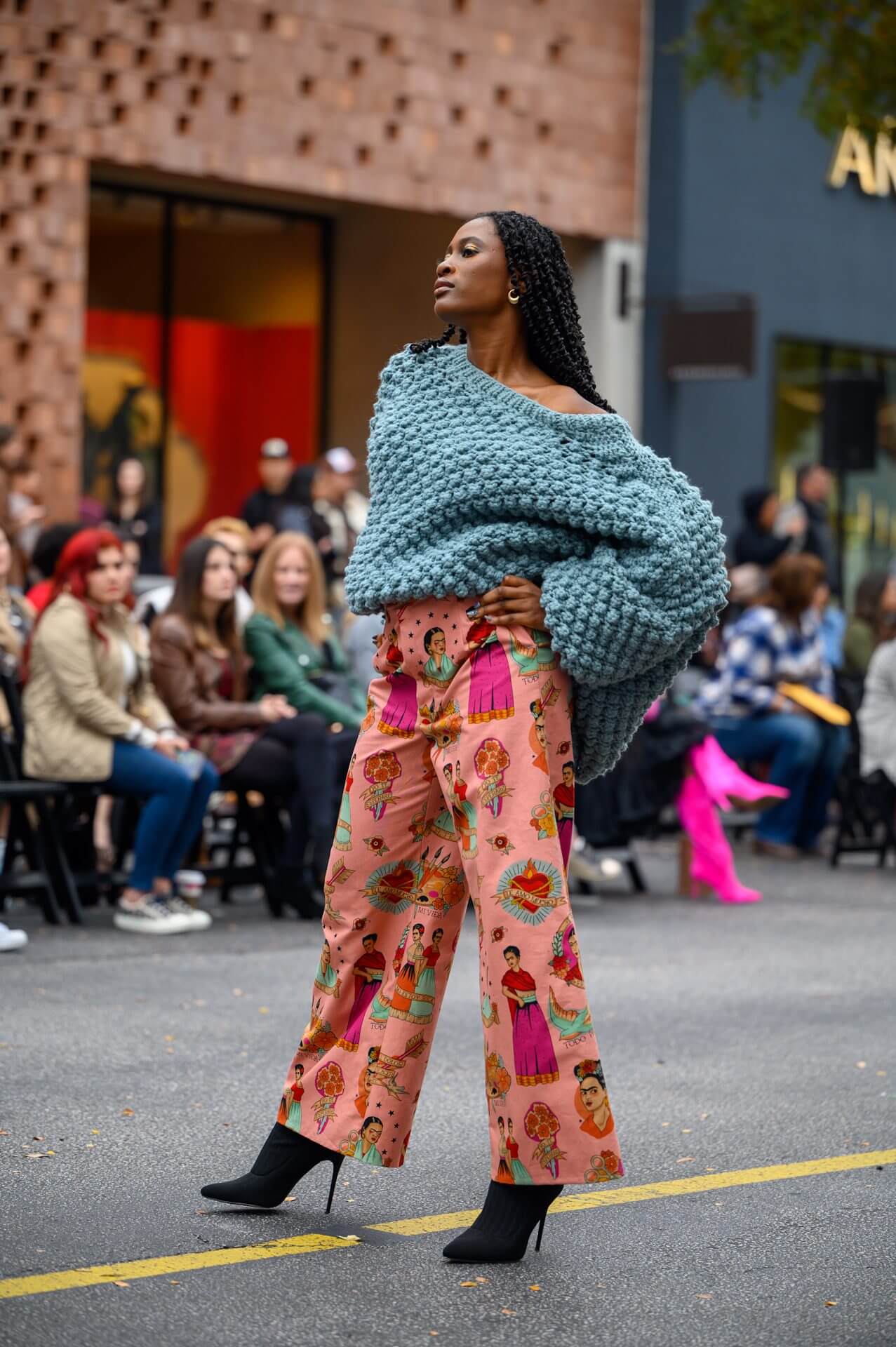 Model wearing a chunky teal sweater and floral pants on a runway.